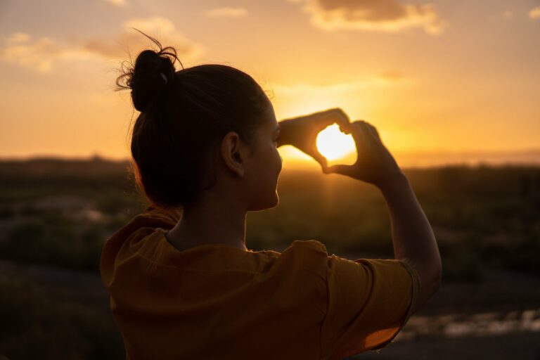 Women forming a heart shape with her hands in front of a sunrise