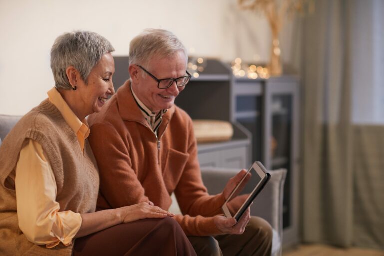 Elderly man and woman smiling at a tablet device.