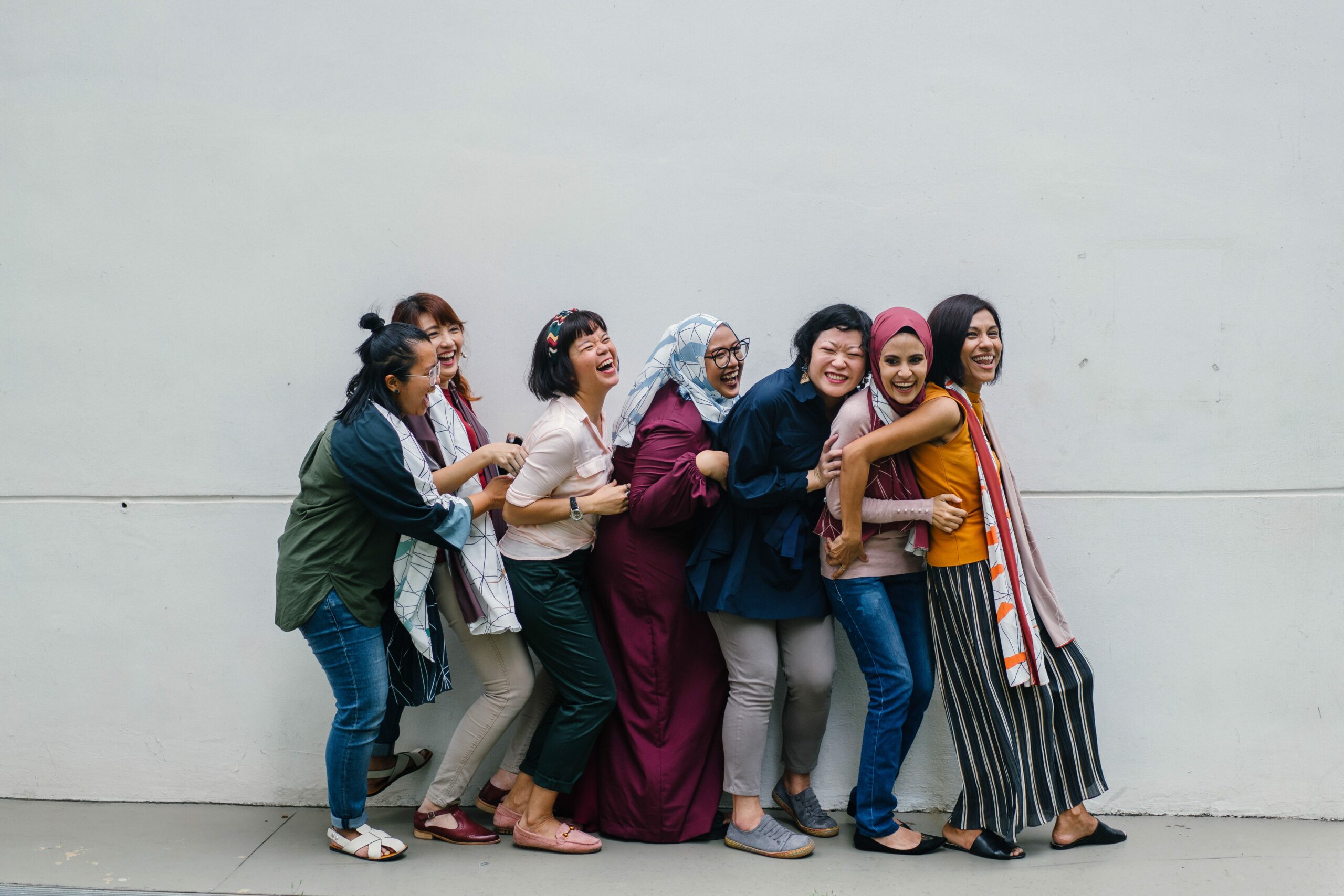 Women in a line against a wall leaning on each other and laughing.