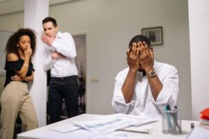 Man covering his face with his hands and in distress while colleagues watch